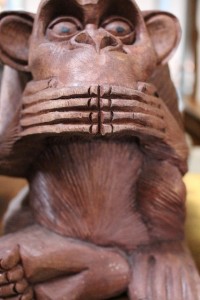 A carved, wooden monkey with its hands covering its mouth.